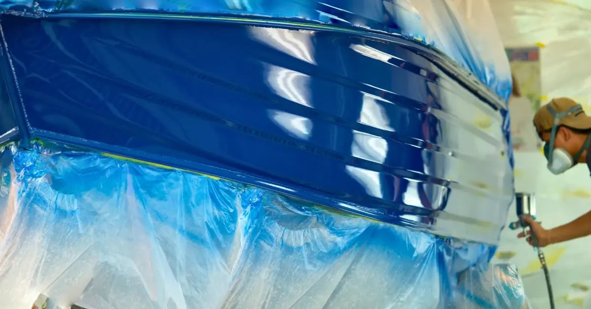 A person spray painting a smaller boat in a shop