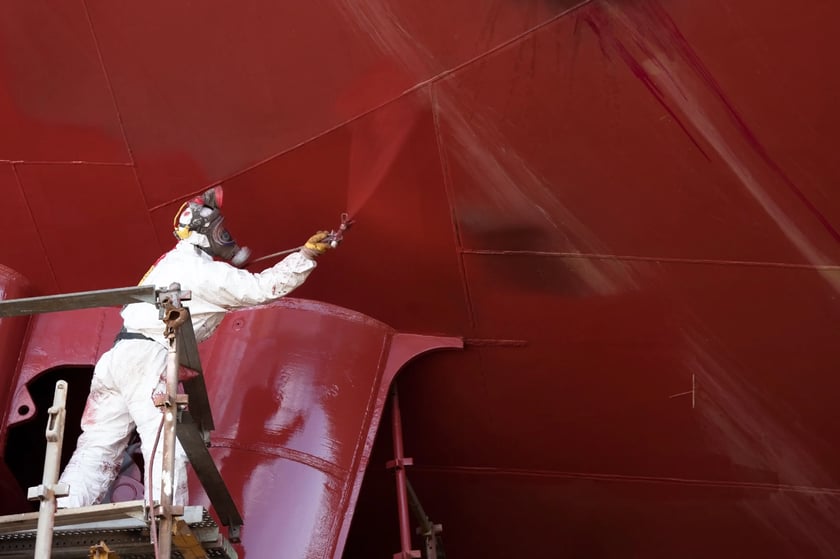 A person spray painting a large marine ship